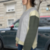 Sudadera tricolor gris con mangas verdes y detalles beige, estilo casual, combinada con jeans en entorno urbano.
