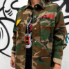 Detalle de sobrecamisa militar camuflaje mujer con bolsillos delanteros y parches decorativos.