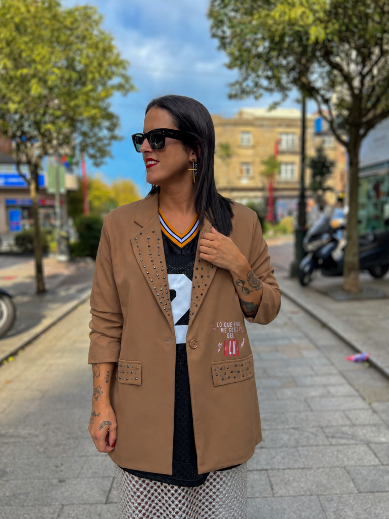 Modelo luciendo la Blazer Alma Camel con detalles de tachuelas metálicas y estampado exclusivo sobre fondo camel.