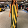 Mujer luciendo un vestido maxi de rayas verticales amarillo y verde oliva, sin mangas y con zapatillas negras, en un entorno urbano.