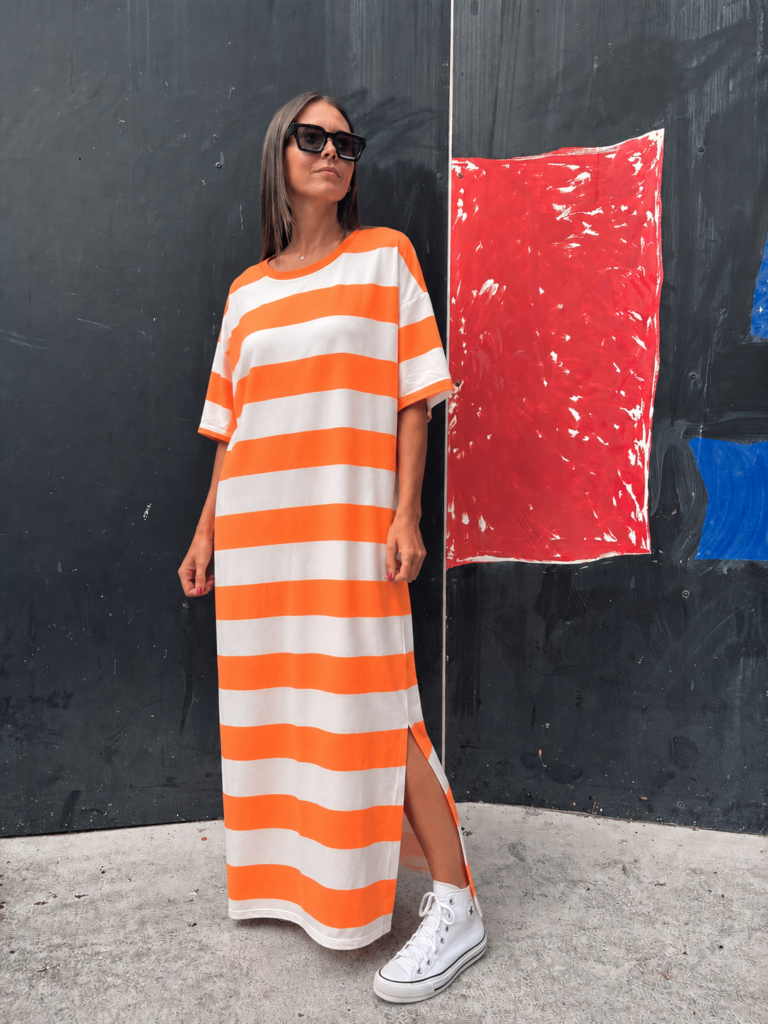 Mujer con vestido maxi sunset tipo camiseta de rayas horizontales naranja y blanco, combinado con zapatillas blancas.
