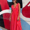 Mujer luciendo el Vestido Flamingo, un vestido maxi de rayas rosa y rojo con escote en V y tirantes con lazadas.