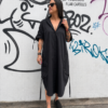 Mujer luciendo un vestido maxi negro antracita de estilo oversize con escote cuadrado y bolsillos laterales en un entorno urbano.