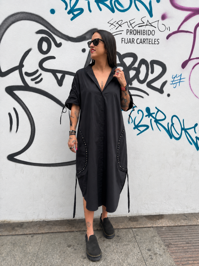 Mujer luciendo un vestido maxi negro antracita de estilo oversize con escote cuadrado y bolsillos laterales en un entorno urbano.