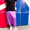 Falda midi satinada en color lila con caída fluida y acabado brillante, combinada con camiseta negra de estilo casual urbano.