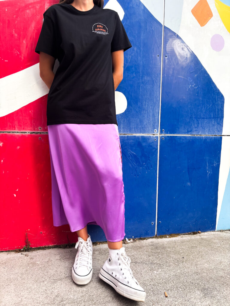 Falda midi satinada en color lila con caída fluida y acabado brillante, combinada con camiseta negra de estilo casual urbano.