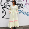 Modelo luciendo el Vestido Largo Lima de Pepa Rodríguez en color blanco con detalles bordados en amarillo flúor, borlas rosas y cinturón ajustable.