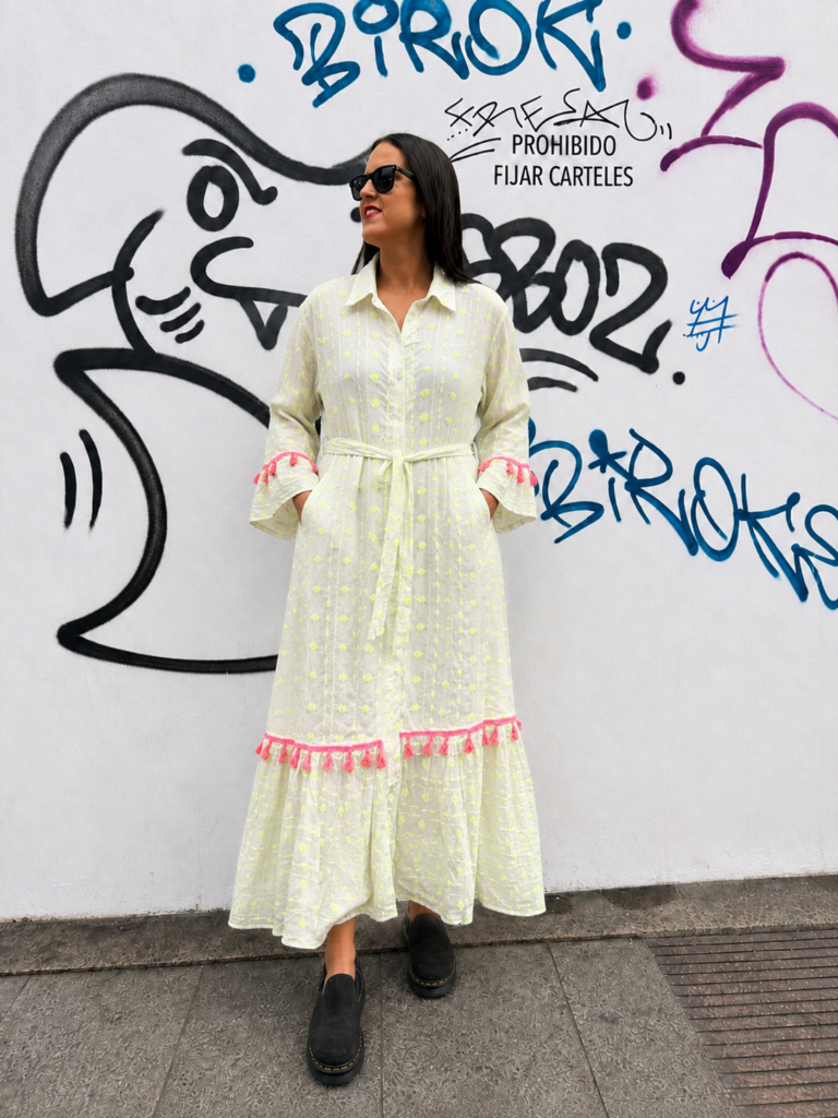 Modelo luciendo el Vestido Largo Lima de Pepa Rodríguez en color blanco con detalles bordados en amarillo flúor, borlas rosas y cinturón ajustable.